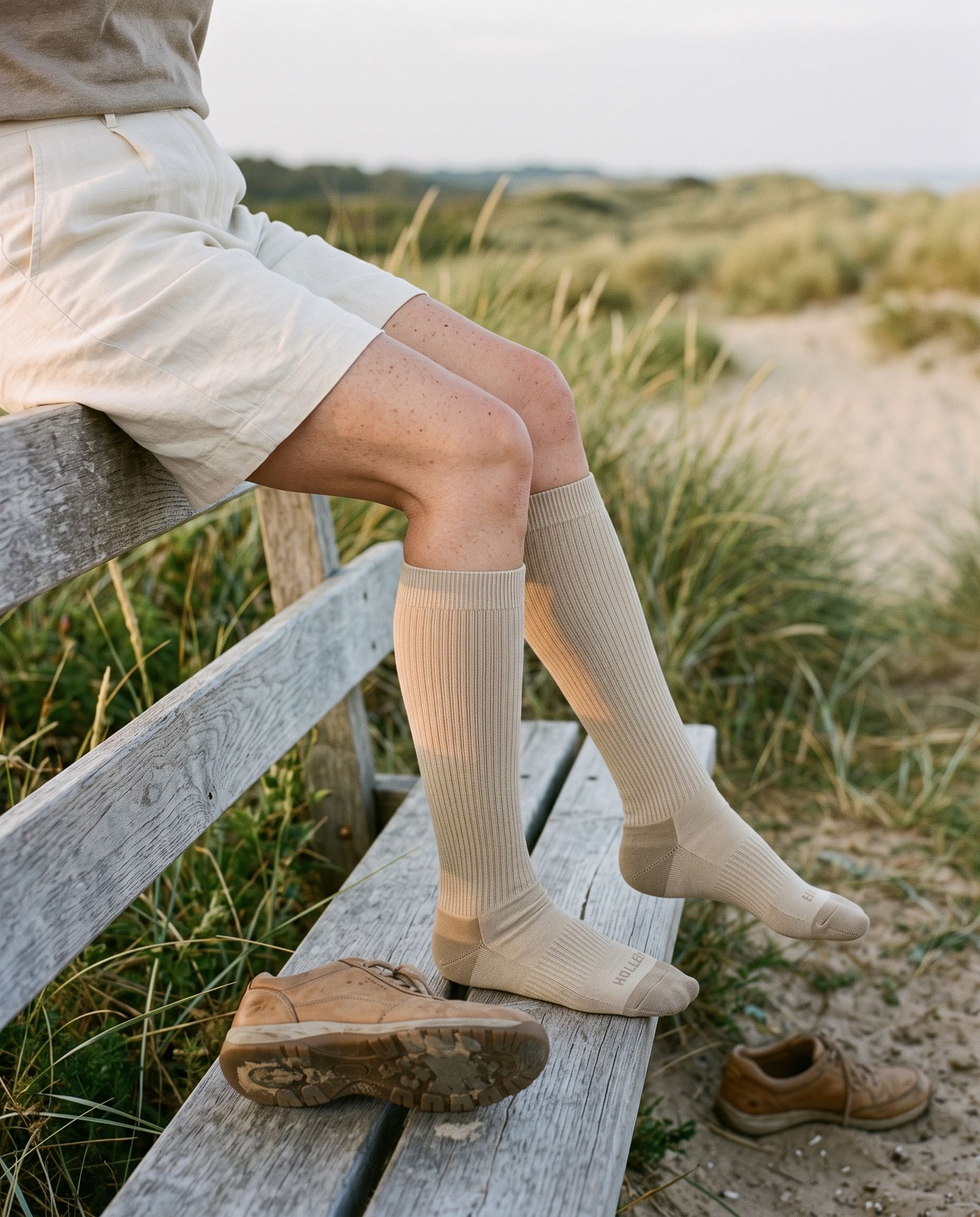 Resting on a weathered bench by coastal dunes in oat Hollen socks, walking shoes off